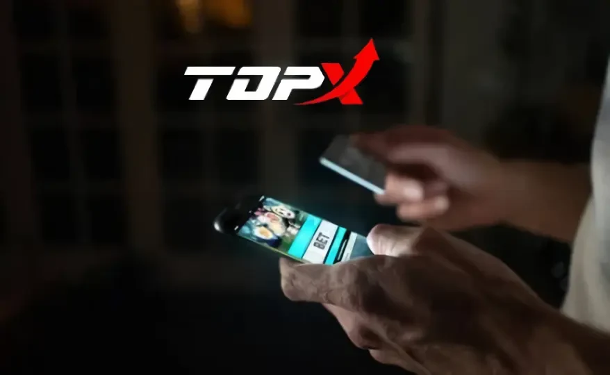 Mãos usando um celular com a tela de um cassino, ao lado do logotipo da TopX